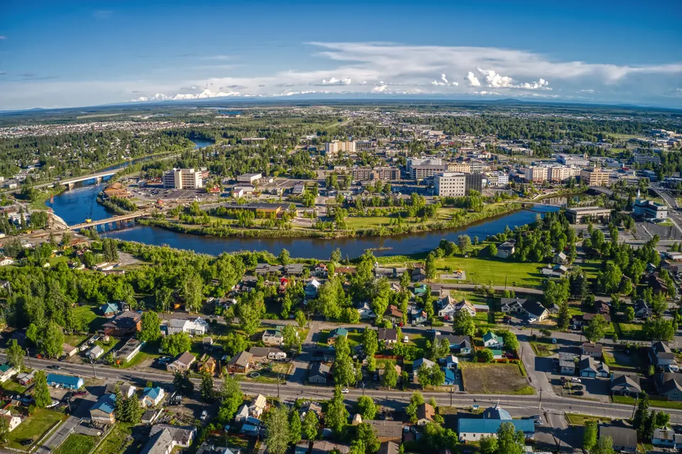 Luftbild einer Stadt mit Wohnhäusern, Bäumen und einem Fluss, über den mehrere Brücken führen.