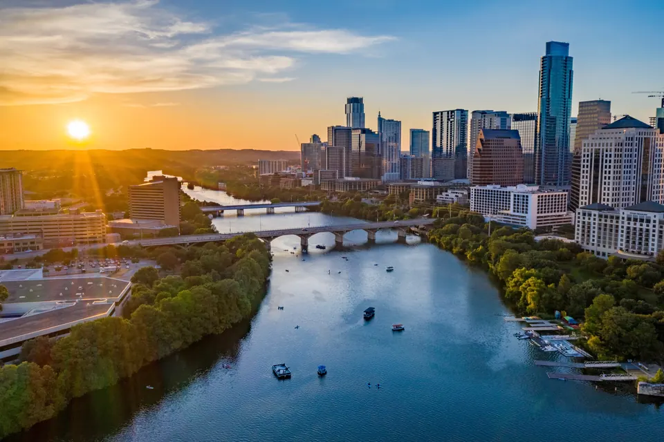 Blick über einen breiten Fluss und mehrere Brücken auf die Skyline von Austin im warmen Abendlicht.
