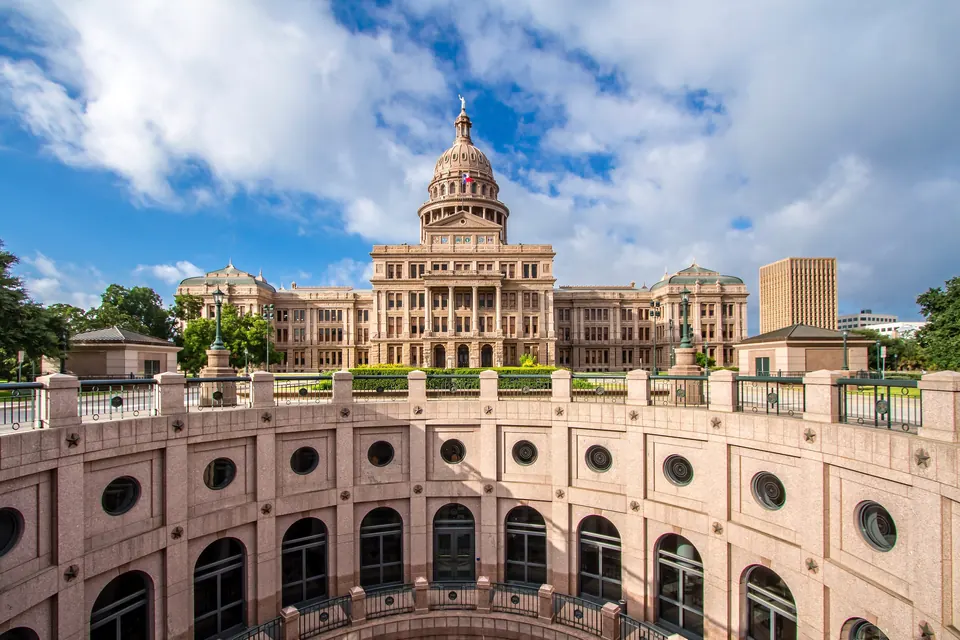 Das Texas State Capitol mit seiner Kuppel unter Wolken, im Vordergrund die Brüstung eines runden, offenen Hofs mit Bogenfenstern.