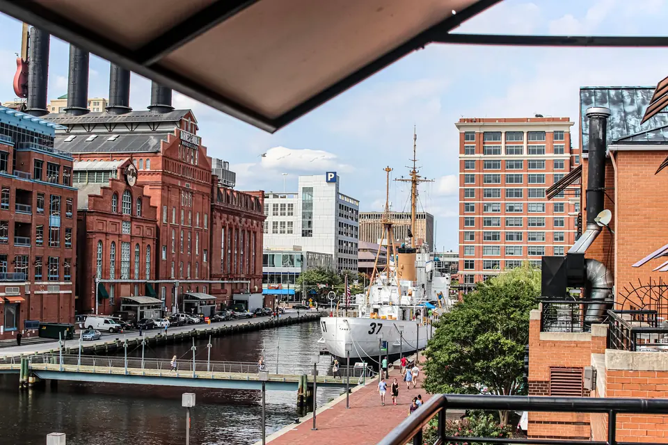 Ein weißes Küstenwachschiff mit der Nummer 37 am Bug liegt an einer Promenade, links ein Hafenbecken und rote Backsteingebäude mit hohen Schornsteinen.