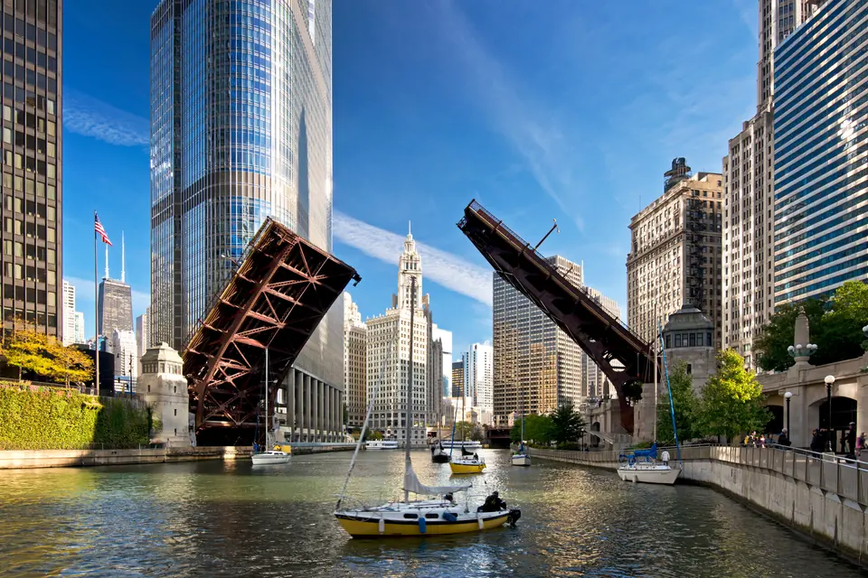 Zwei hochgeklappte Brückenflügel über dem Chicago River, darunter fahren Segelboote, ringsum Hochhäuser.