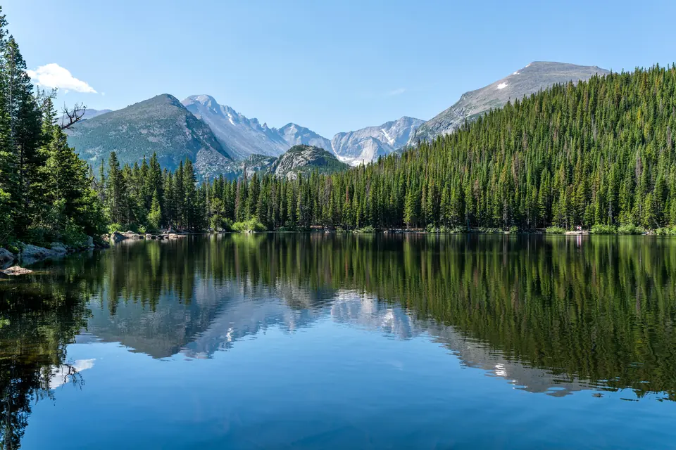 Stiller Bergsee, in dem sich Nadelwald und felsige Gipfel spiegeln.