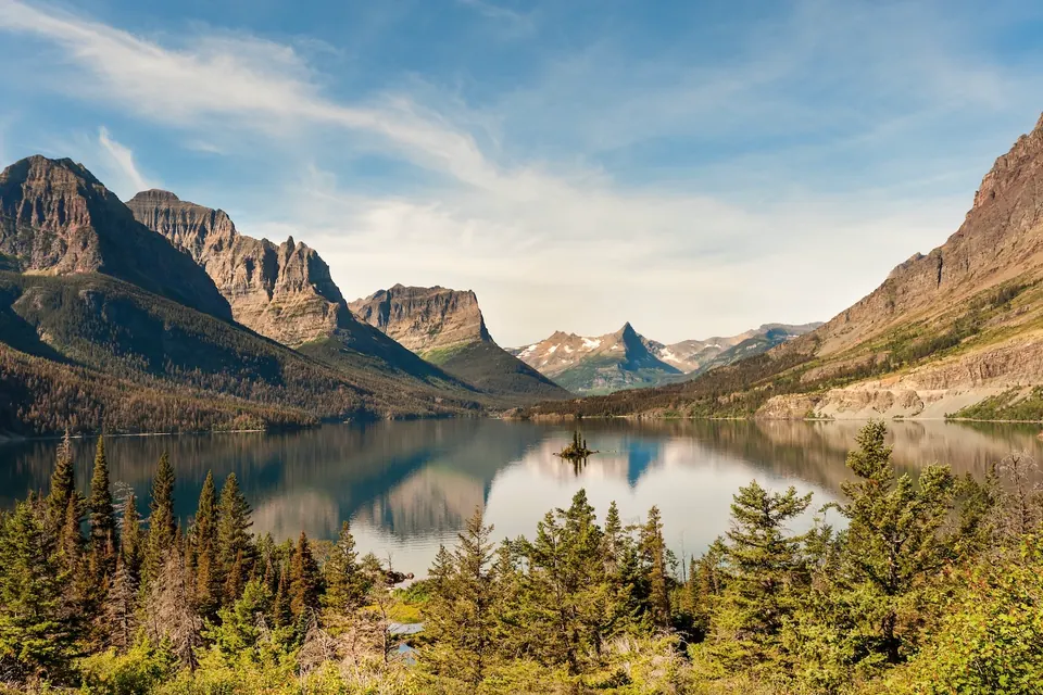Blick über den St. Mary Lake auf eine kleine bewaldete Insel und die dahinterliegenden Berge.