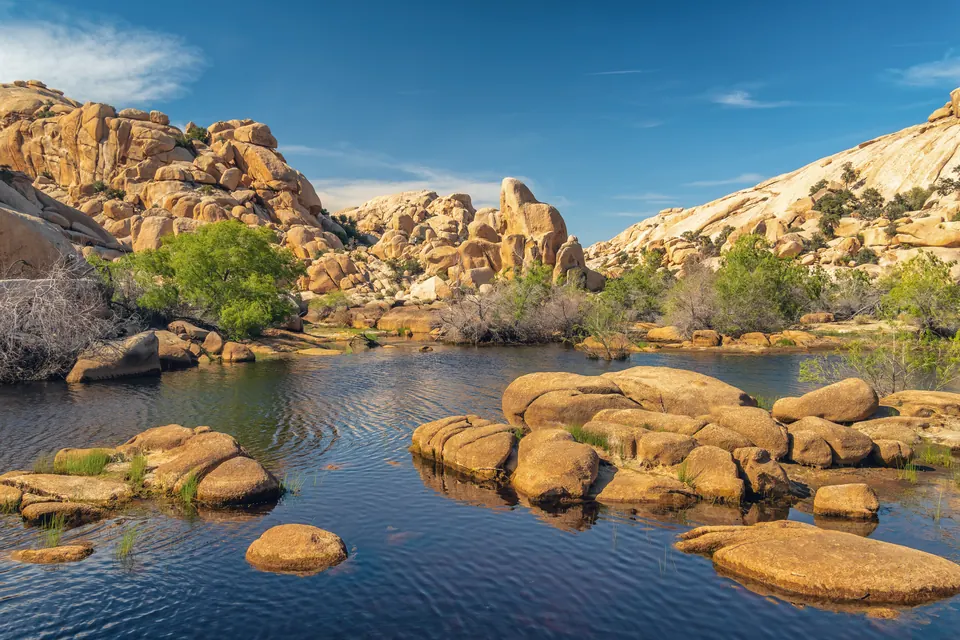 Wasser zwischen gelblich beleuchteten Granitfelsen und einzelnen grünen Sträuchern am Barker Dam.