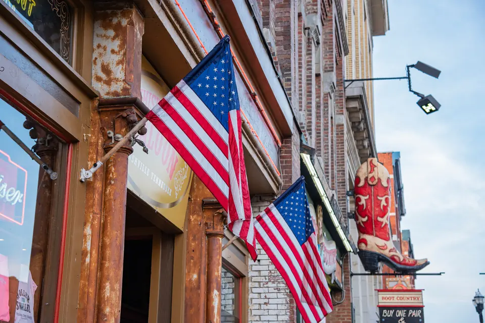 Backsteinfassaden mit zwei amerikanischen Flaggen über einem Eingang, auf einem Schild steht Nashville Tennessee, weiter hinten hängt ein großer roter Cowboystiefel als Ladenschild.