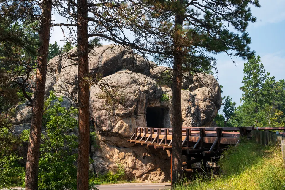 Tunnelöffnung in einem Granitfelsen zwischen Kiefern, davor eine hölzerne Brückenkonstruktion.