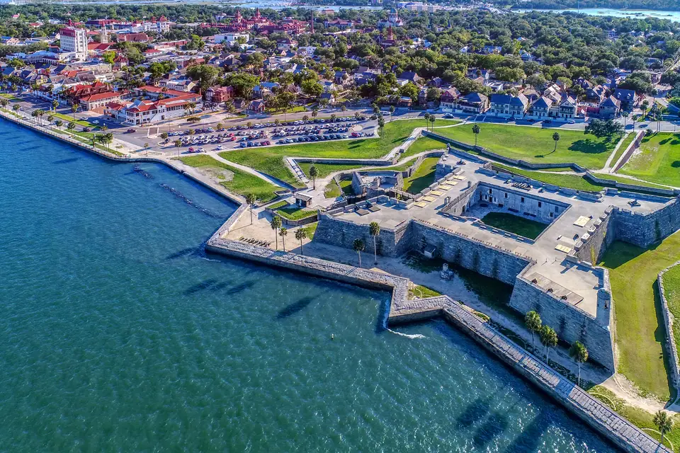 Luftbild einer sternförmigen Festung aus grauem Stein mit spitzen Bastionen direkt am Wasser. Dahinter liegen Rasenflächen, ein Parkplatz und die Häuser der Altstadt.