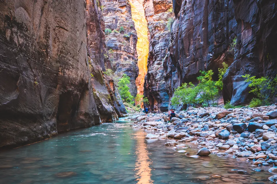Sehr enge Schlucht mit senkrechten, dunkelroten Sandsteinwänden, durch die ein Fluss über Kiesel fließt.